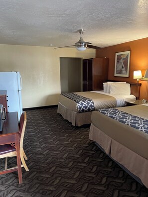 A hotel room with two beds, a desk, a refrigerator, a ceiling fan, and a painting on the wall. - Vernals Best Value Inn (Vernal)