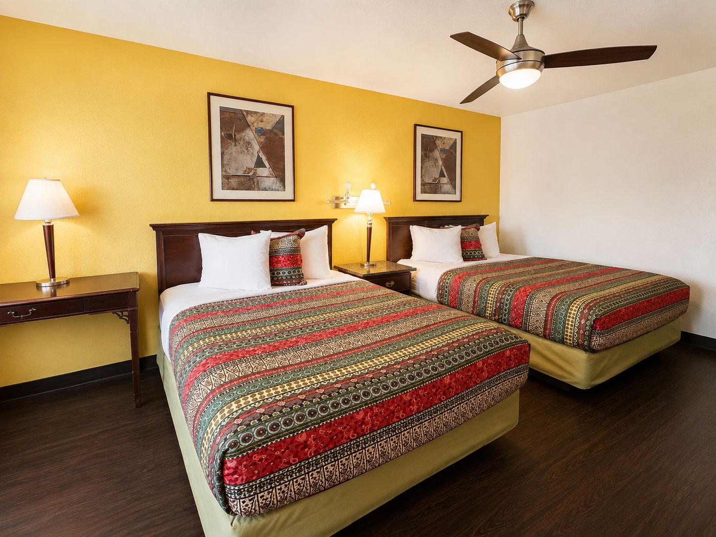 Habitación de hotel con dos camas, ventilador de techo y obras de arte en las paredes.