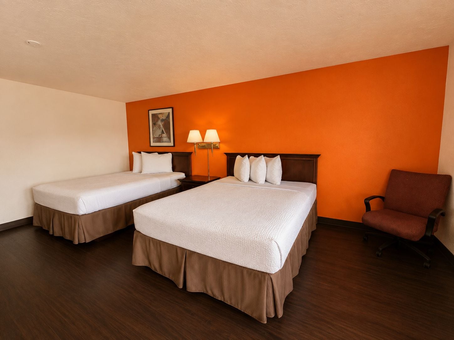 Habitació d'hotel amb dos llits, una cadira i un quadre a la paret.
