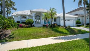 A single-story house with a white exterior, a front porch, and a well-maintained lawn. - Stunning Sunsets, Spacious Waterfront Home (Marco Island)