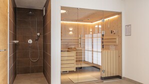 A modern shower area with a glass partition, wooden cabinets, and a small seating area. - Superior chalet # 2B with sauna (Uttendorf)