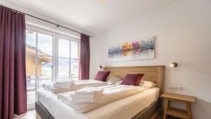 A bedroom with a large bed, a wooden headboard, a small bedside table, and a window with curtains. - Superior chalet # 4A with sauna (Uttendorf)