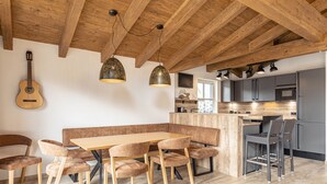 A modern kitchen with a wooden ceiling, a dining area with a wooden table and cushioned chairs, and a kitchen island with bar stools. - Superior chalet # 4A with sauna (Uttendorf)