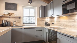 A modern kitchen with grey cabinets, a wooden countertop, a built-in oven, and a window with blinds. - Superior chalet # 4A with sauna (Uttendorf)