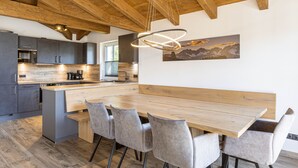 Una cocina moderna con vigas de madera, una isla central, armarios grises y una zona de comedor con una mesa y sillas de madera.
