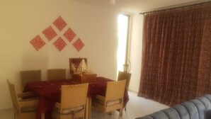 A dining area with a table and chairs, a decorative wall piece, and a window with curtains. - Bright apartment with garden (الكورة)