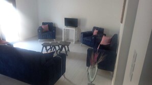 A living room with dark blue sofas, a coffee table, and a TV on a white stand. - Bright apartment with garden (الكورة)