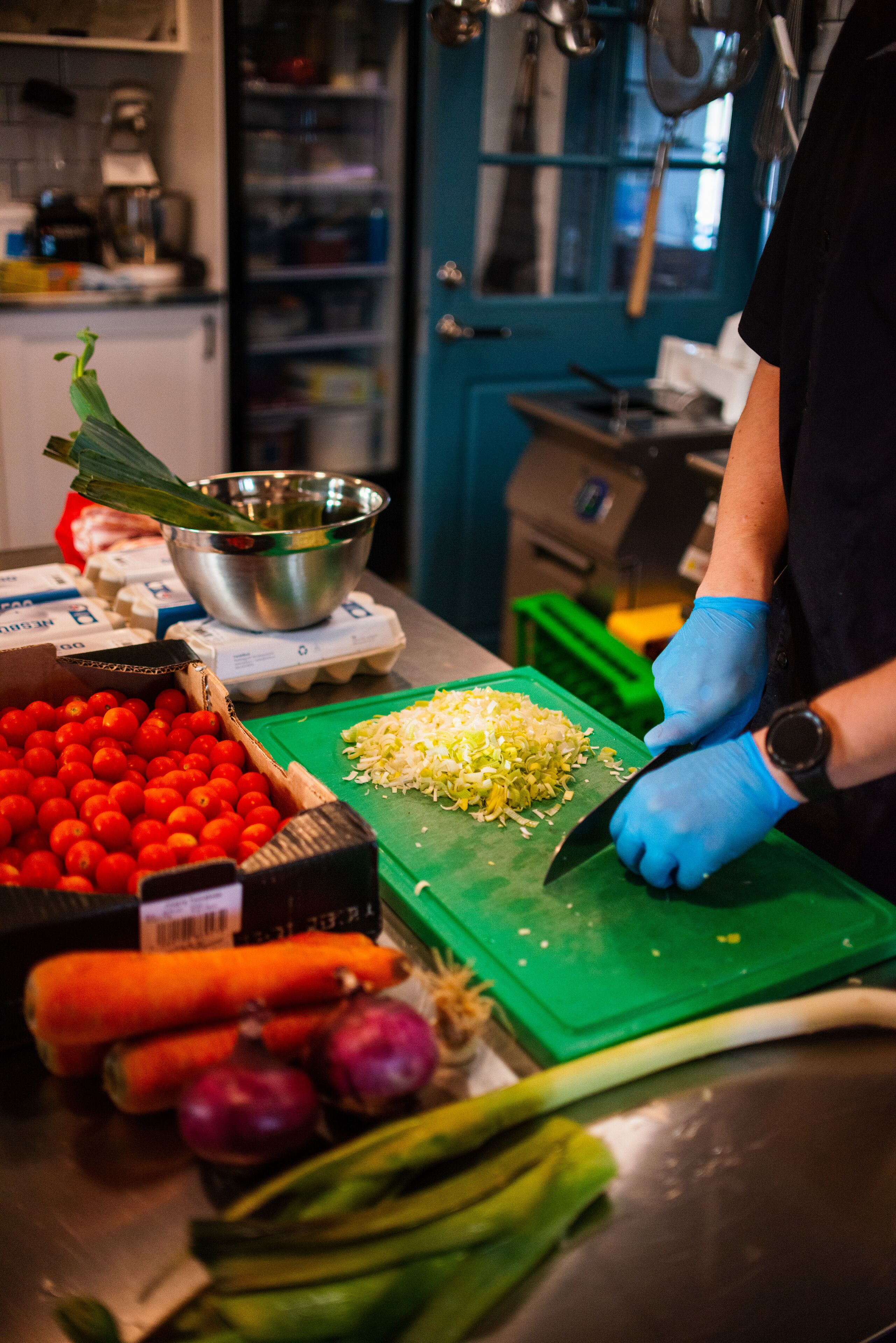 A kitchen with a cutting board, vegetables, and a person preparing food.