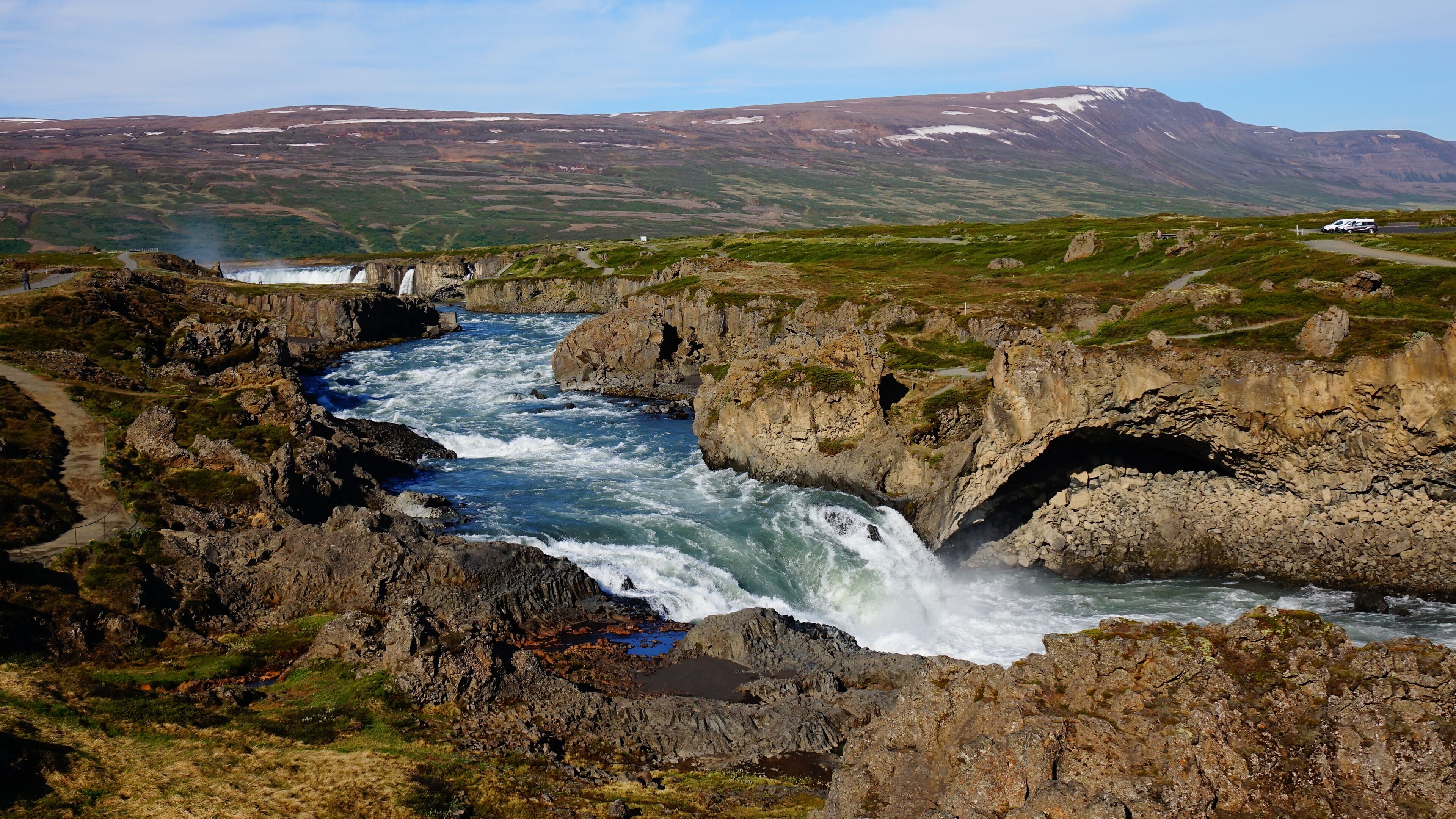 A river flowing through a rocky landscape with a waterfall and a mountainous backdrop.