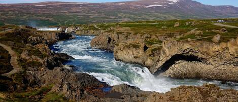A river flowing through a rocky landscape with a waterfall and a mountainous backdrop.