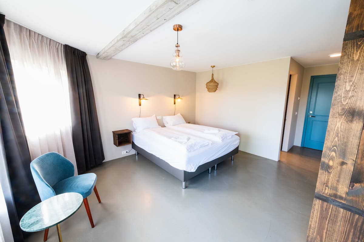 A modern hotel room with a large bed, a blue chair, and a wooden door.