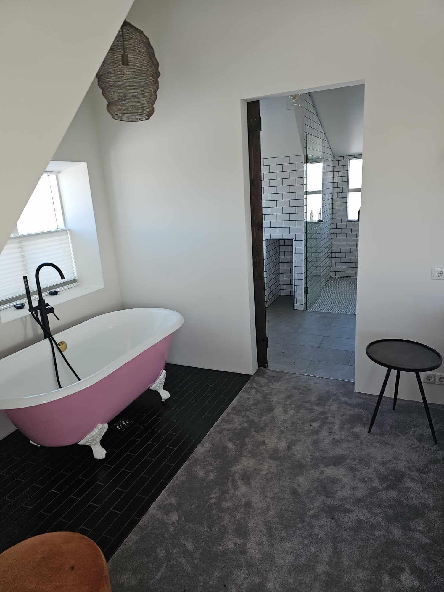 A modern bathroom with a freestanding pink bathtub, a black sink, and a small round table.
