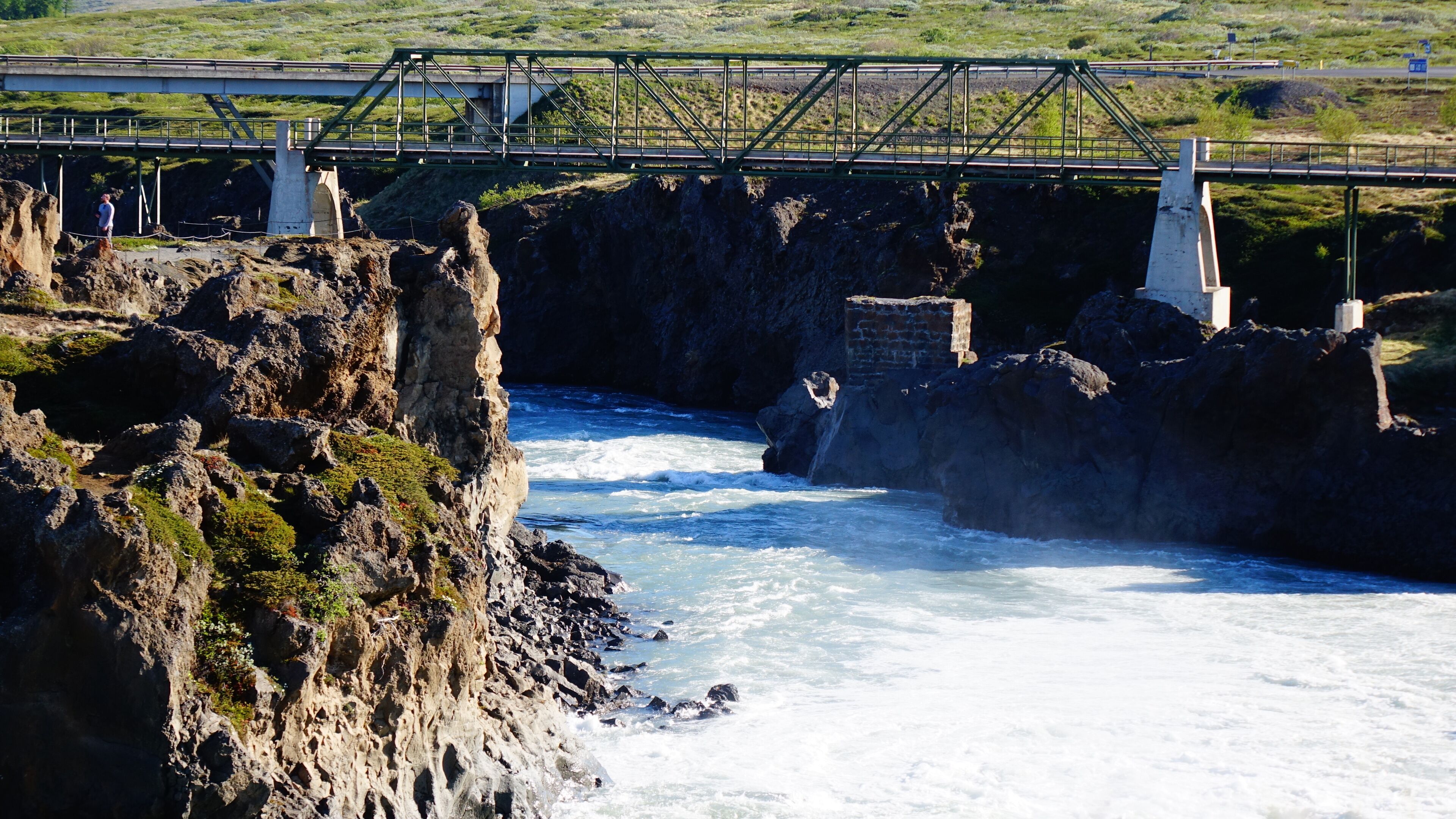 Un puente sobre un río pedregoso, con vistas del paisaje circundante.
