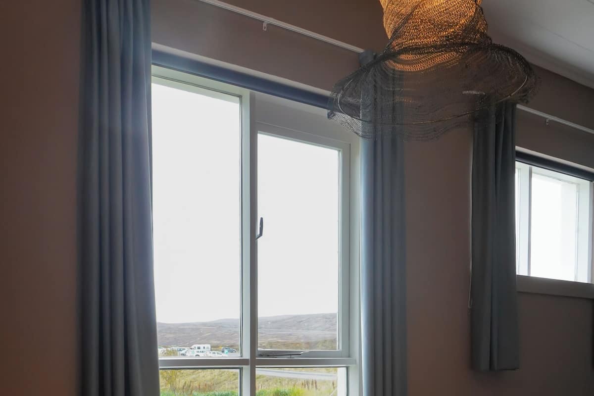 A hotel room with a large window, a bed with a wooden headboard, and a view of the outdoors.