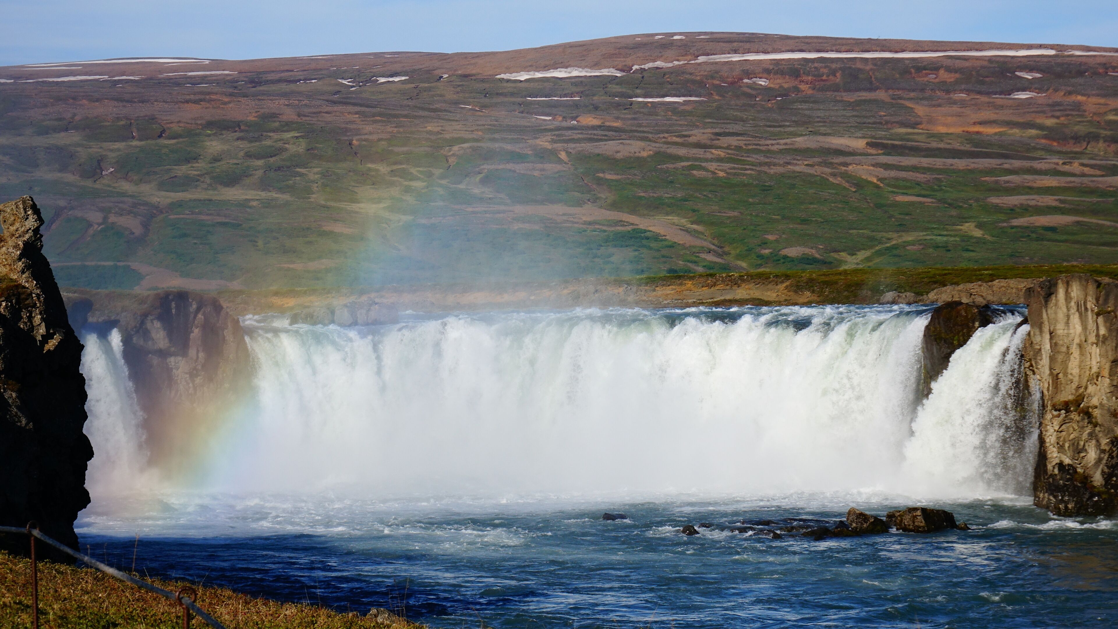 A waterfall with a rainbow, surrounded by a rugged landscape.