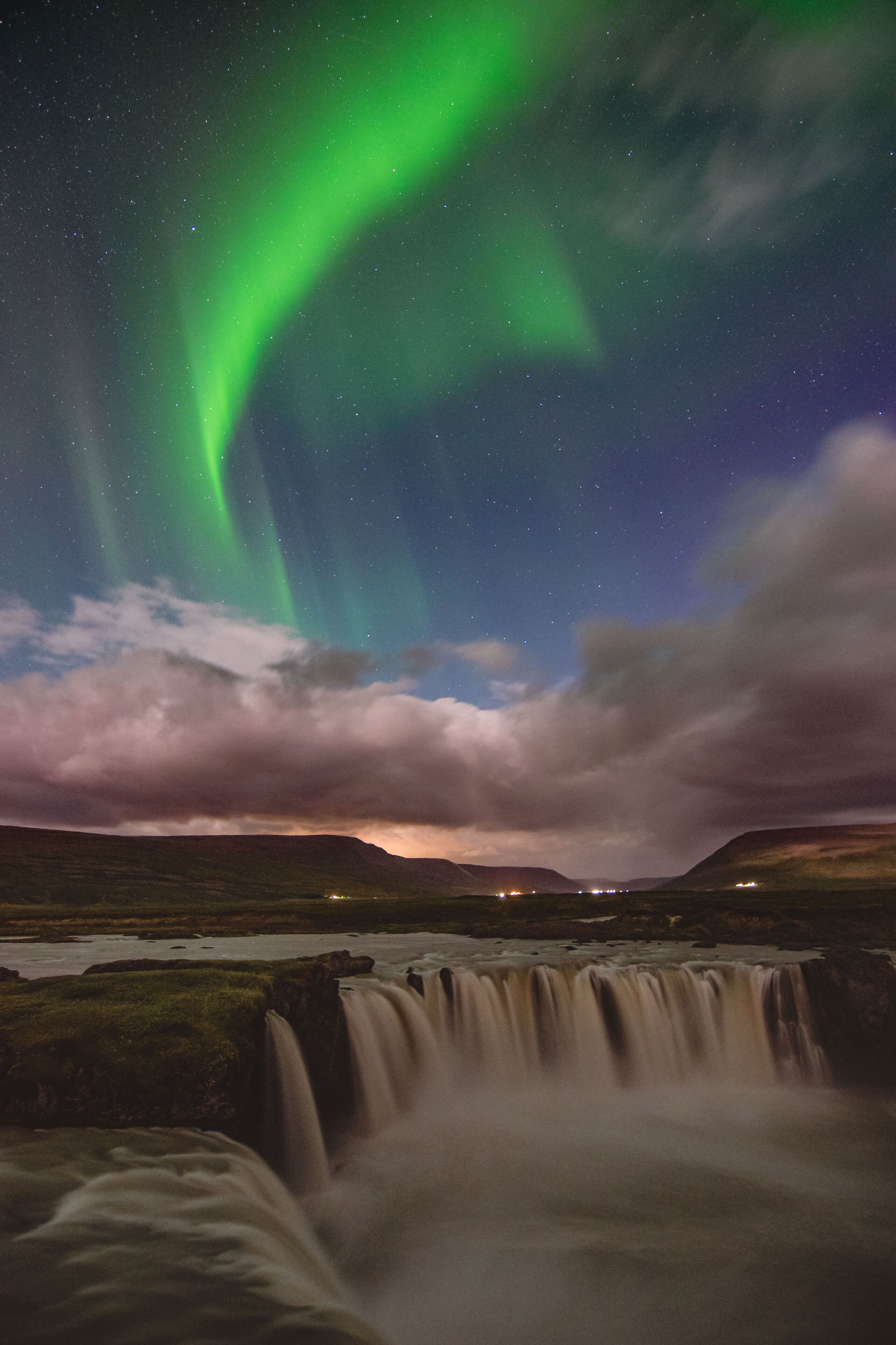 A waterfall with a night sky featuring the Northern Lights.