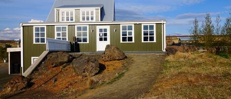 A two-story building with a green exterior and white trim, featuring multiple windows and a large rock formation in front.