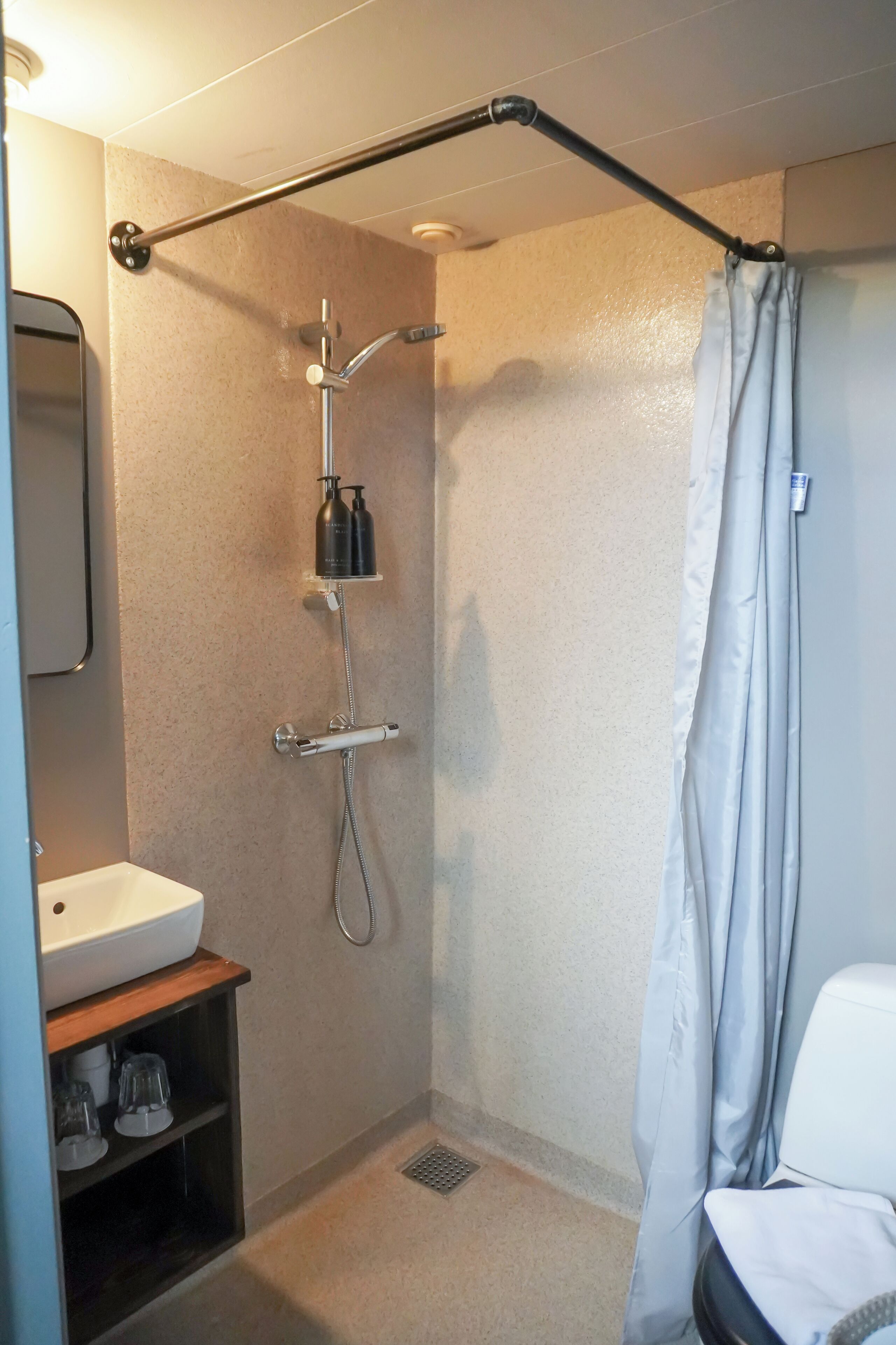 A small, well-lit bathroom with a shower, a sink, and a mirror.