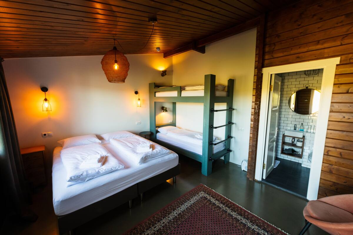 A room with two beds, wooden walls, and a small kitchenette.