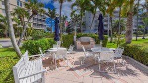 An outdoor patio with white metal furniture, palm trees, and a view of a hotel building in the background. - Minute walk to the Beach! Florida Condo with screened in porch. (Stuart)