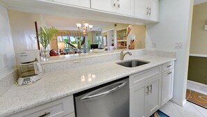 A modern kitchen with white cabinetry, a stainless steel dishwasher, and a granite countertop. - Minute walk to the Beach! Florida Condo with screened in porch. (Stuart)