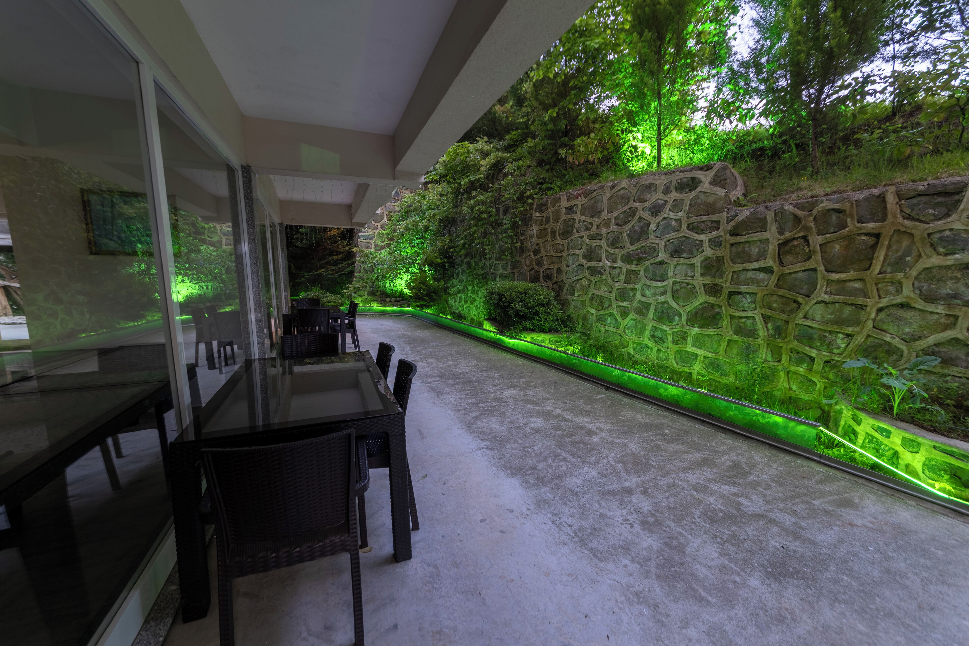 A modern outdoor dining area with a stone wall and green lighting.