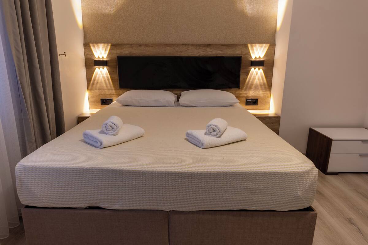 Een tweepersoonsbed met twee handdoeken, een houten hoofdbord en wandlampen.