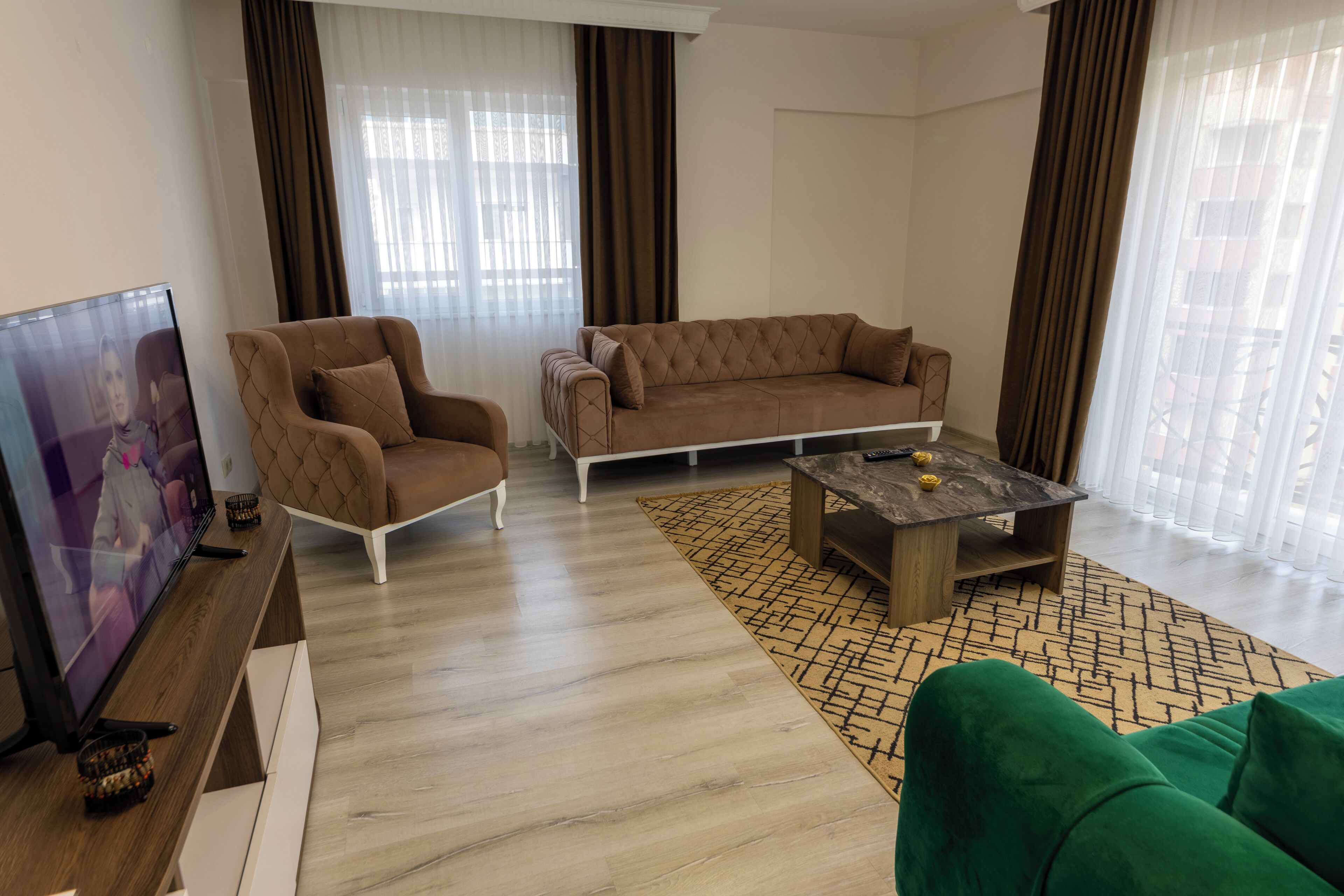 Una sala de estar con un sofá marrón, un sofá verde, una mesa de centro de madera y un televisor sobre un mueble de madera.