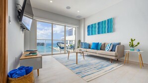 A modern living room with a sofa, a coffee table, and a view of the sea through large windows. - Harbour House (Oranjestad)