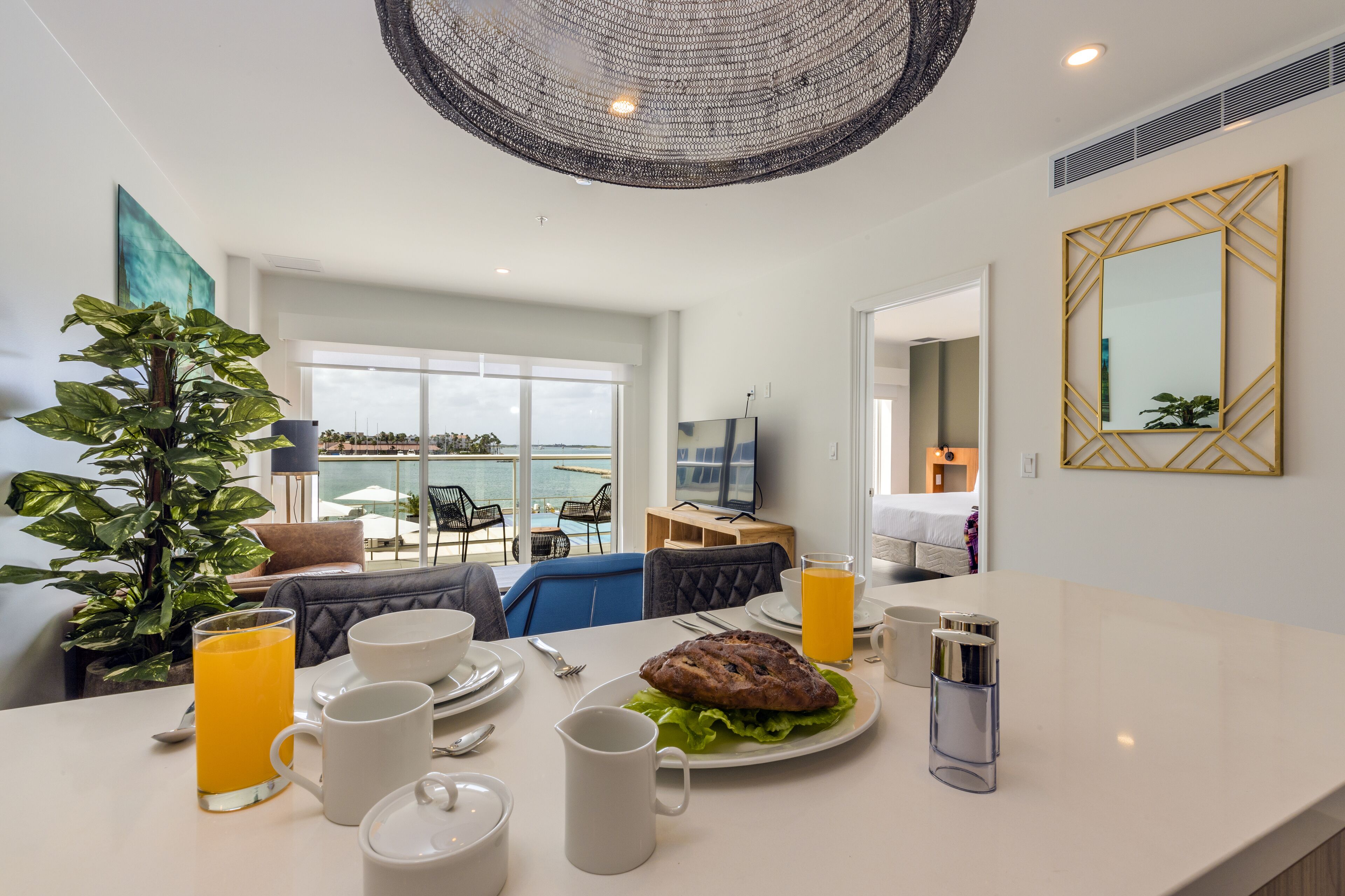 Ein modernes Hotelzimmer mit Essbereich, ausgestattet für ein Frühstück, einem großen Fenster mit Meerblick und einer gemütlichen Sitzecke mit Pflanze.