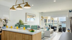 A modern kitchen with a central island, a dining area with a sofa and chairs, and a view of the sea through large windows. - Harbour House (Oranjestad)