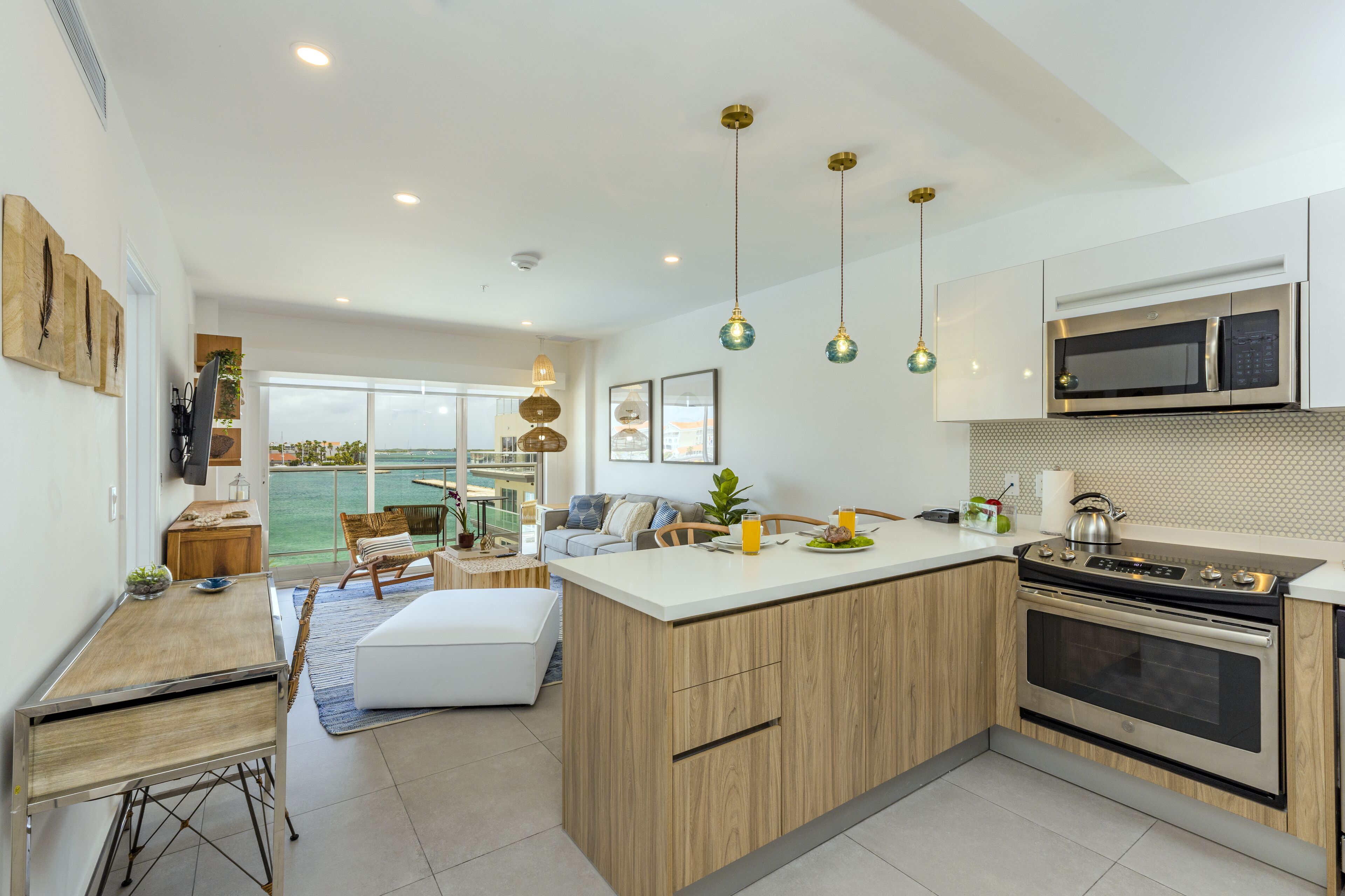 Une cuisine moderne dotée d’un îlot central, d’appareils électroménagers en acier inoxydable et de luminaires suspendus.