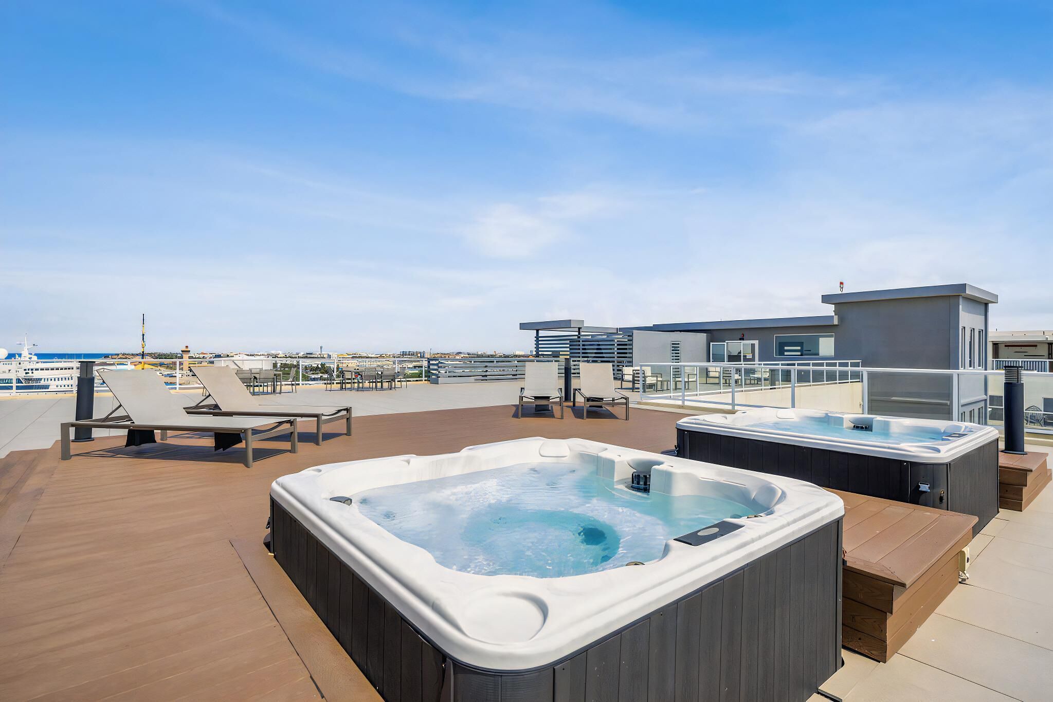 Eine Dachterrasse mit zwei Whirlpools, Liegestühlen und Meerblick.
