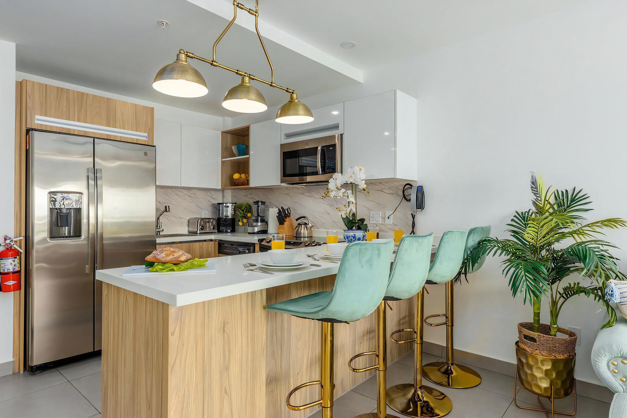 A modern kitchen with a stainless steel refrigerator, wooden cabinets, a marble countertop, and a bar area with green barstools.