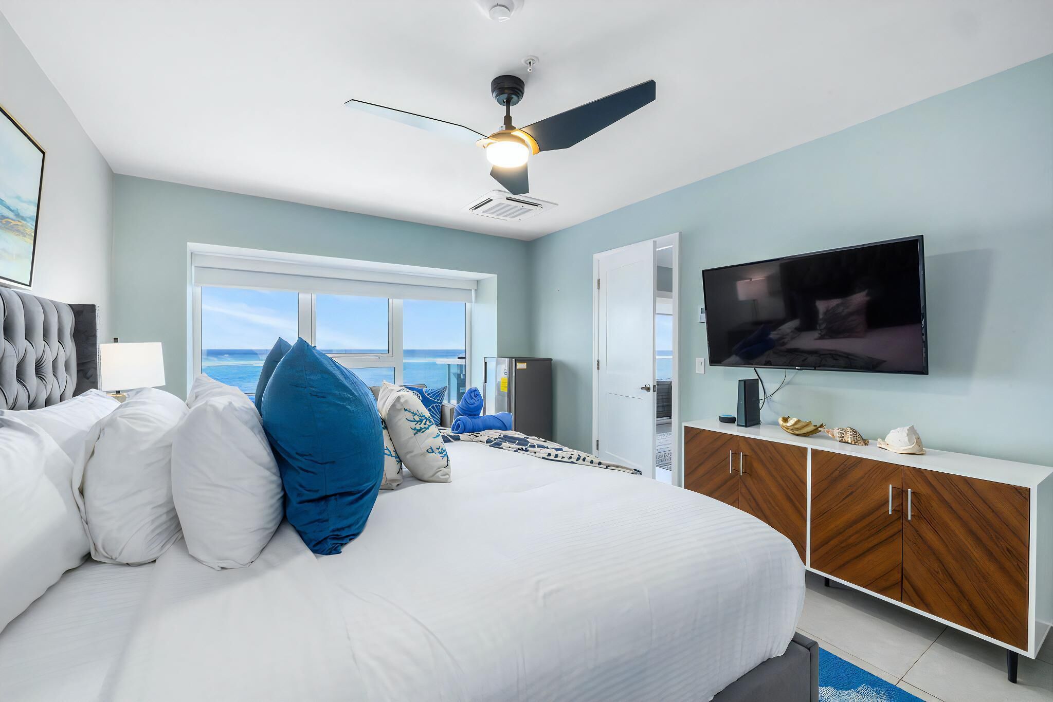 Een slaapkamer met een bed, een plafondventilator, een televisie en uitzicht op de oceaan.