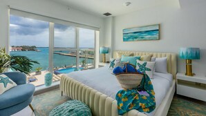 A hotel room with a large bed, a view of the sea, a painting, and a plant. - Harbour House (Oranjestad)