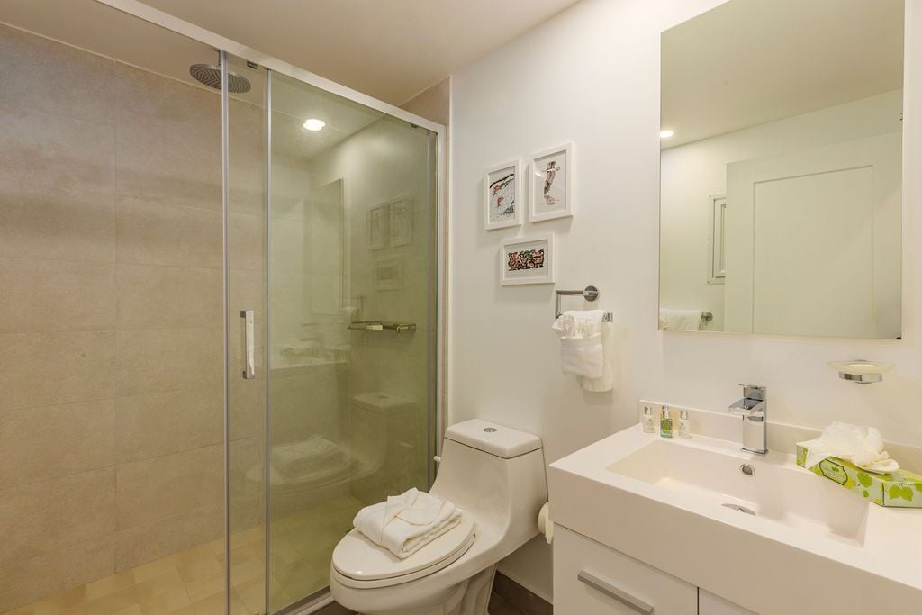 A modern bathroom with a glass-enclosed shower, a white toilet, and a sink with a mirror above it.