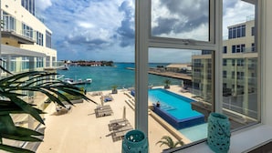 A view from a hotel room overlooking a swimming pool, lounge area, and marina with boats. - Harbour House (Oranjestad)