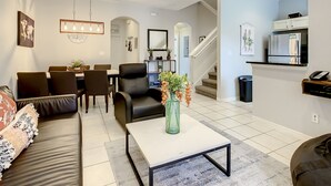 Ein modernes Wohnzimmer mit Sofa, Couchtisch und Essbereich. Eine Treppe führt zur oberen Etage.