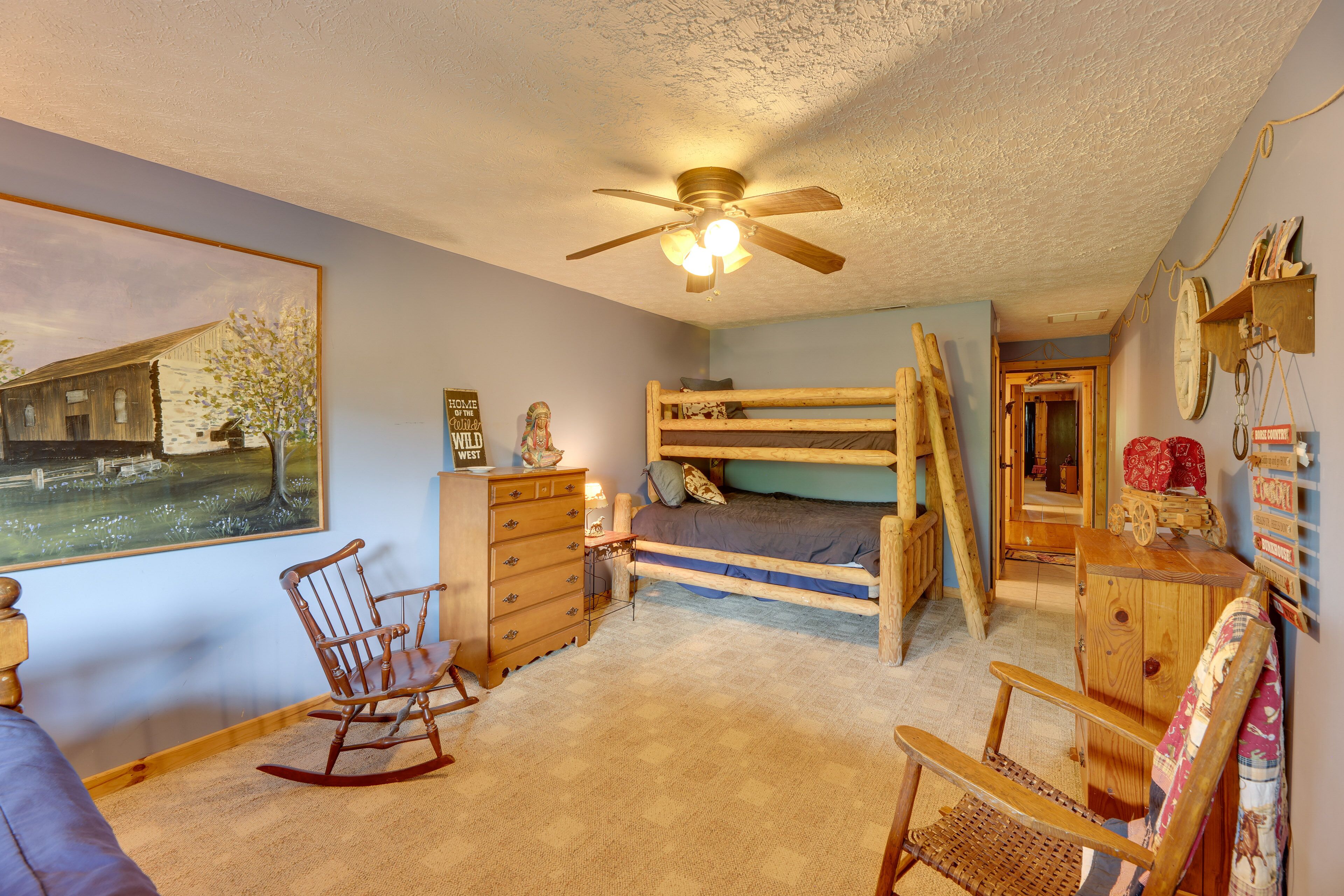 A rustic bedroom with a bunk bed, a rocking chair, a desk, and a ceiling fan.