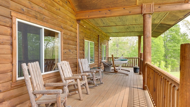A wooden deck with rocking chairs and a table, overlooking a forested area.