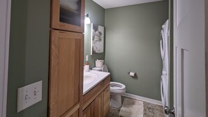 A bathroom with a wooden vanity, a toilet, and a shower area. - Charming Couple's Cottage close to Lake Michigan, Silver lake, and Stoney Lake (Shelby)