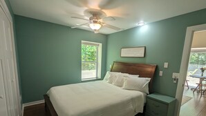 A bedroom with a bed, a nightstand, a ceiling fan, a window, and a door. - Charming Couple's Cottage close to Lake Michigan, Silver lake, and Stoney Lake (Shelby)