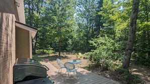A wooden deck with a barbecue grill, a table, and two chairs. - Charming Couple's Cottage close to Lake Michigan, Silver lake, and Stoney Lake (Shelby)