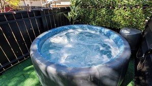 A hot tub with a blue rim, surrounded by a black fence and green foliage.