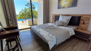 Un dormitorio con cama, mesitas de noche, un escritorio y vistas a una piscina y vegetación.