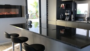 Una cocina moderna con encimera negra, electrodomésticos de acero inoxidable y tres taburetes negros.