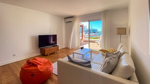 Una sala de estar moderna con un televisor de pantalla plana, un sofá, una mesa de centro y un sillón orejero rojo.