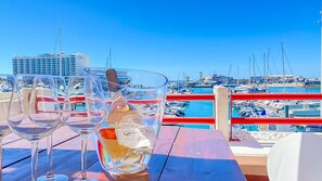 Ein Yachthafen mit Booten, einem wolkenlosen, blauen Himmel und einem Tisch mit Weingläsern und einer Weinflasche.