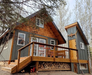 Une cabane dotée d’une terrasse en bois, d’un escalier menant à un porche et d’une pile de bois de chauffage à l’extérieur.